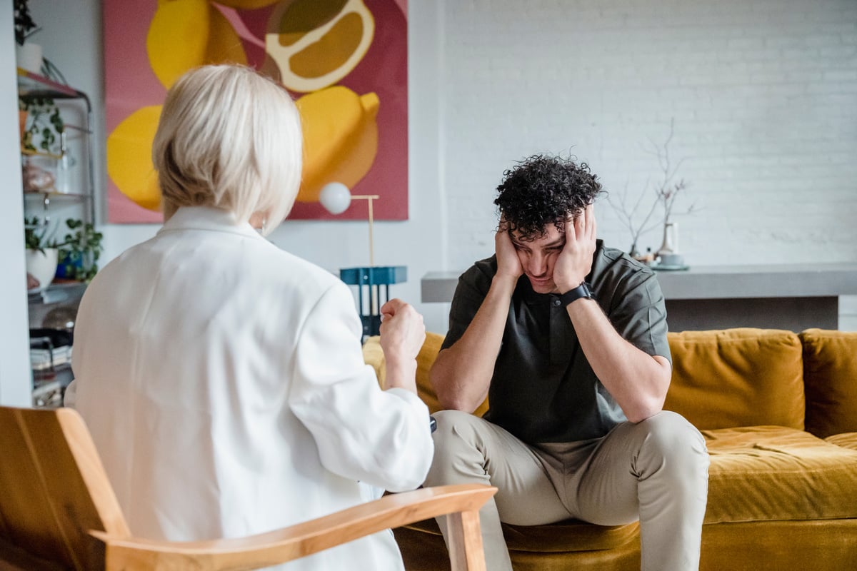 a person sitting on a couch with their head in their hands and another person sitting next to them