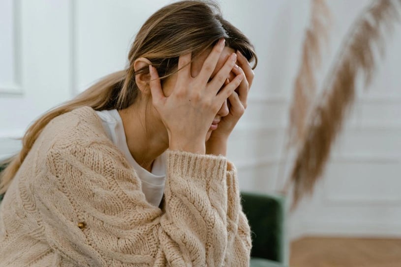 a person covers their face with their hands while sitting on a couch